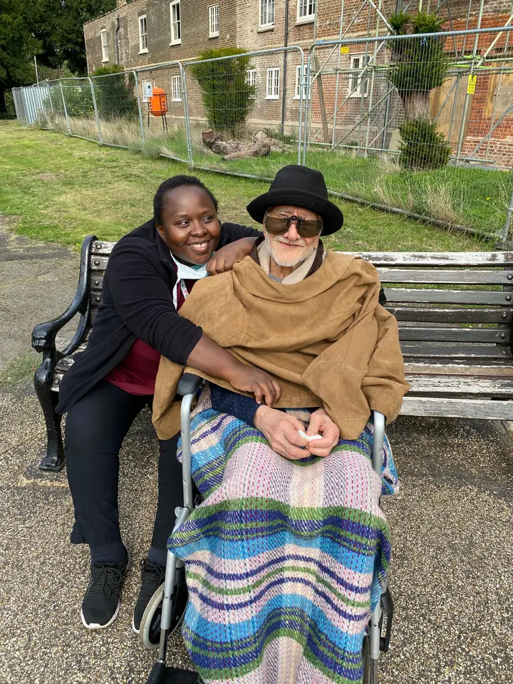 A Muzaana care worker sitting beside an older man using a wheelchair outdoors