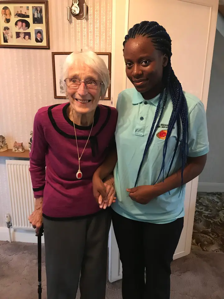 An older woman and a Muzaana care worker standing together in a living room