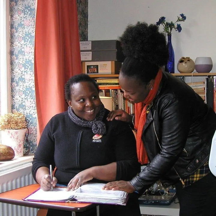 Two members of the Muzaana team working through paperwork together, one writing notes.